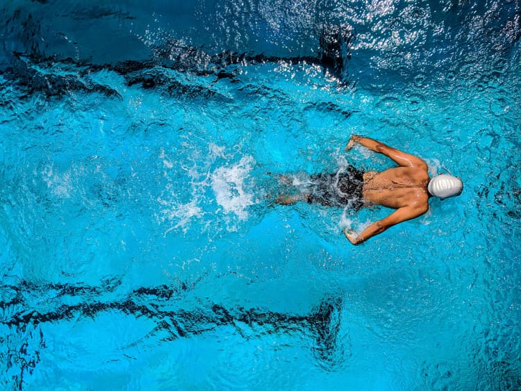 A competitive swimmer immersed in a clear, blue swimming pool, executing the butterfly stroke with precision. His arms are extended behind him, slicing through the water, and his face is submerged as he propels forward.